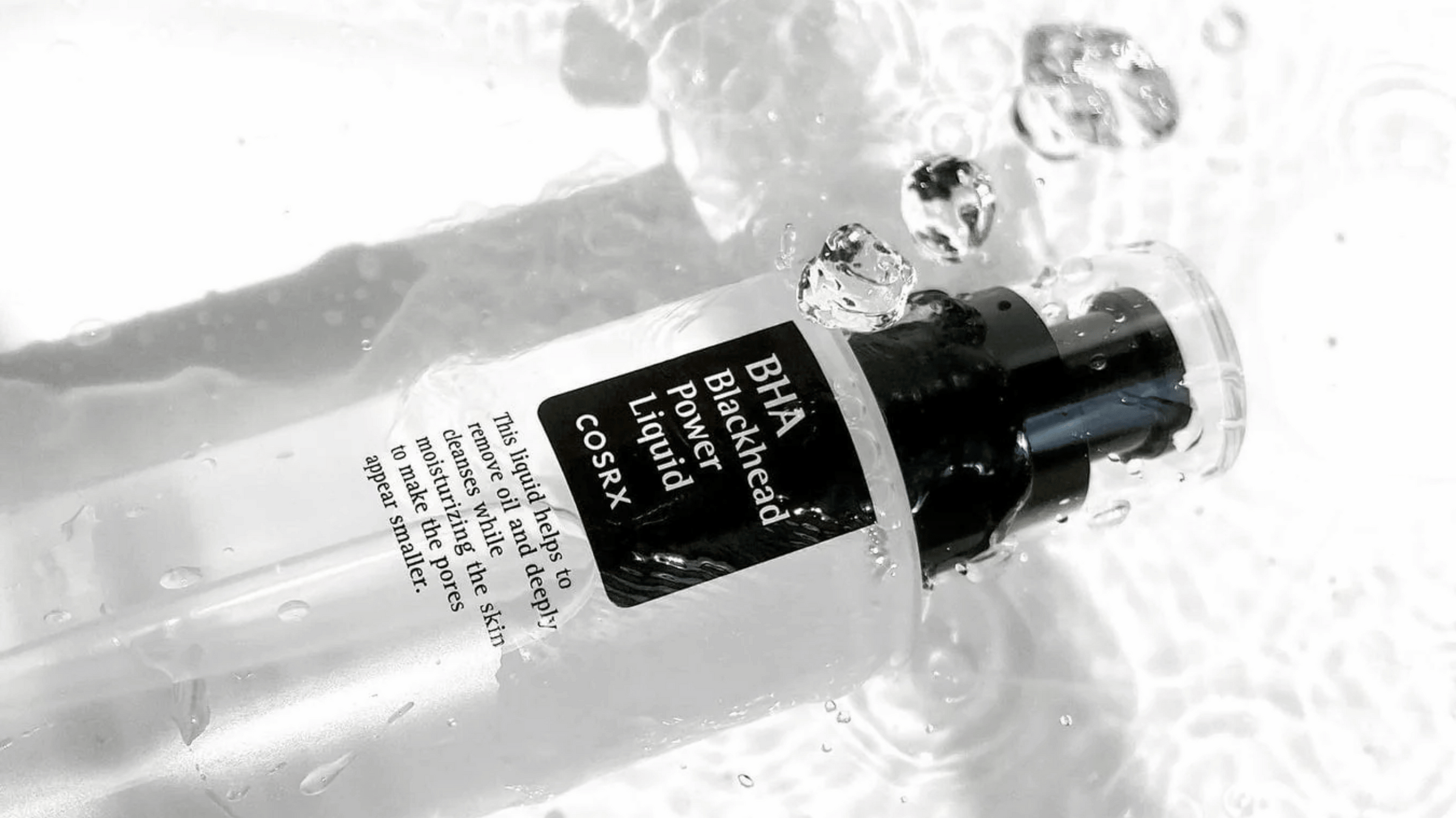 COSRX BHA Blackhead Power Liquid i en elegant genomskinlig flaska. Designad för att minska pormaskar, rengöra på djupet och återfukta huden. Perfekt för en klarare hudton och mindre synliga porer. Produkten omges av stänk av vatten för en fräsch känsla.