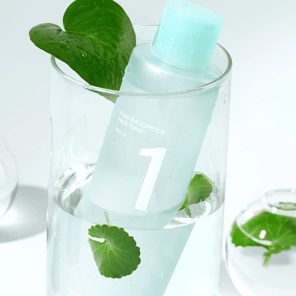 En flaska med No.1 Pure-Full Calming Herb Toner placerad i ett glas med vatten och gröna blad. Flaskan har en ljusblå kork och en etikett med texten "Pure-full Calming Herb Toner" samt "300ml". Produkten ser fräsch ut med vatten och växtlighet i bakgrunden, vilket ger en lugnande och naturlig känsla.